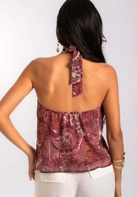 Haut halter en motif paisley violet avec un col froncé, un lien à l'arrière et un tissu transparent. Associé à un short en lin blanc.