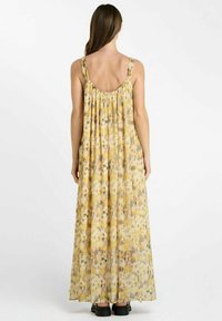 Maxi-jurk van lichtgewicht gele stof met een bloemenpatroon. Heeft een geraffineerde achterkant, dunne bandjes en een vloeiende silhouet.