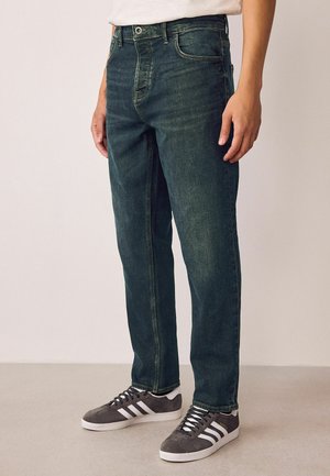 Dunkelblaue Jeans mit geradem Schnitt, ausgestattet mit einem klassischen Fünf-Taschen-Design und subtiler Ausbleichung, kombiniert mit grauen Sportschuhen.