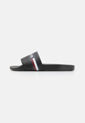 Sort slidesandal med bred rem med røde, hvide og blå striber og delvis hvid tekst på remmen.