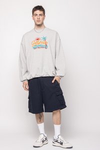 Felpa grigia con una grafica colorata "California", abbinata a pantaloni cargo blu navy. Il modello indossa calze bianche e sneakers con dettagli neri.