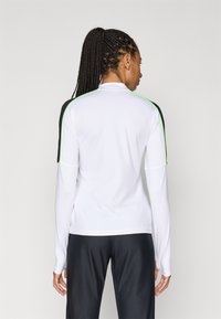 Long-sleeve athletic top in white with black sleeves and green accents. Smooth fabric, fitted design, and high neckline.