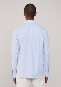 Camisa de manga larga a rayas azul claro, hecha de algodón, con cuello abotonado, pliegue en la parte posterior y dobladillo redondeado.