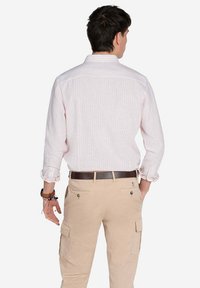 Camisa de rayas en rosa claro y blanco con mangas largas, puños abotonados y un cuello estándar, combinada con pantalones cargo caqui y un cinturón marrón.
