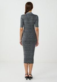 Robe midi tricotée en bleu foncé avec des rayures verticales. Manches courtes, col montant et silhouette ajustée. Texture lisse et léger éclat.