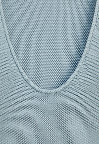 Vaaleansininen neulepaita, jossa on pyöreä kaula-aukko, ja se sisältää tekstuuripinnan sekä sileät reunat. Kangas näyttää pehmeältä ja joustavalta.