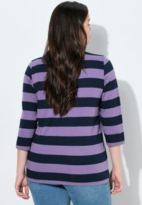 Lilla og marineblå stribet skjorte med trekvartærmer, med en afslappet pasform og blød tekstur, kombineret med lyseblå jeans.