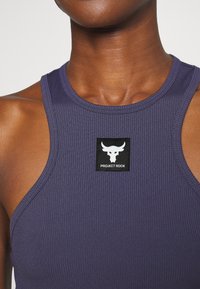 Primer plano de una persona que lleva una camiseta sin mangas de canalé morada con un logo en blanco y negro de Project Rock centrado en el pecho.