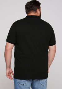 Czarna koszulka polo wykonana z bawełny, z kołnierzykiem i krótkimi rękawami. Tył ma gładką teksturę z minimalnymi detalami.