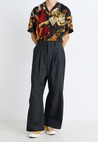 Camisa de manga corta con estampado barroco colorido, combinada con pantalones grises de pierna ancha y cintura alta y zapatillas mostaza.