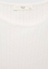 Top bianco lavorato a maglia con una texture a coste, caratterizzato da un sottile motivo a diamante, scollatura rotonda e etichetta con la scritta "MNG HOME."