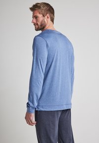 Camisa azul de manga larga con cuello redondo y corte relajado, combinada con pantalones gris oscuro. Tejido ligero con textura suave.