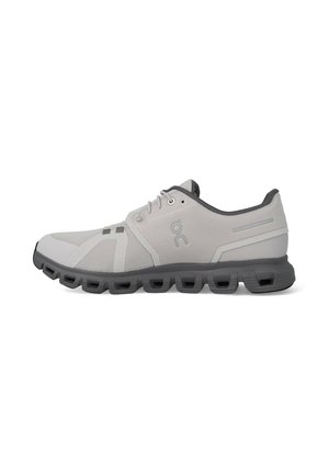 Hellgrauer Sportschuh mit dunkelgrauer Sohle und Mesh-Obermaterial, mit Schnürsenkeln und Markenlogo an der Seite.