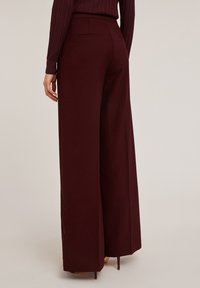 Burgundyröda byxor med vida ben och hög midja, slät yta, två bakfickor och en ren design. Längden når strax ovanför vristen.