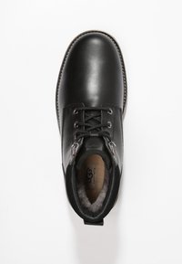 Botín de cuero negro hasta el tobillo con punta redonda, diseño con cordones, suave forro gris y dos acentos metálicos cerca de la parte superior.