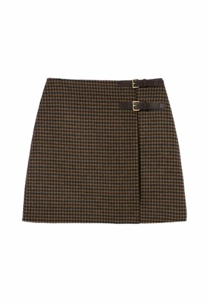 Donna che indossa un maglione beige con cappuccio e laccio, minigonna marrone a quadri con fibbia, calzini grigi al ginocchio, mocassini neri e tiene una pochette nera.