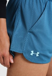 Blå nätaktiga träningsshorts med en lätt textur, som har en rundad fåll och en broderad vit Under Armour-logotyp på den nedre sidan.