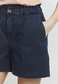 Pantalones cortos azul marino hechos de tela de algodón, con una cintura elástica, cierre de botón en la parte delantera y bolsillos laterales.