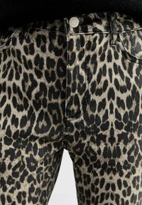 Gros plan sur un jean en denim beige et noir à imprimé léopard avec poches avant et fermeture par bouton argenté.