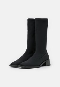 Botines negros con parte superior de tela ajustada, puntera afilada y tacón bajo de bloque. Textura suave con un detallado mínimo y sin herrajes visibles.