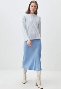 Maglione peloso blu chiaro con strisce bianche diagonali, abbinato a una gonna in satin blu chiaro liscia e stivaletti bianchi con tacco a blocco fino al ginocchio.