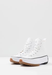 Białe sneakersy za kostkę wykonane z płótna, z czarnym paskiem, unikalną ząbkowan�ą gumową podeszwą oraz metalowymi oczkami na sznurówki.