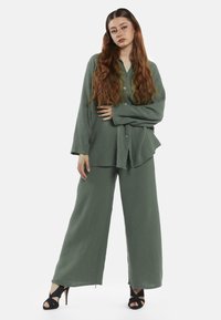 Grøn, struktureret to-delt sæt bestående af en langærmet skjorte med knapper og brede bukser, parret med sorte strop-sandaler.