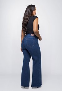 Blauwe denim high-waisted flared jeans met een donkere wassing, voorzien van vier zakken, riemlussen en een gestikt leren label aan de achterzijde.