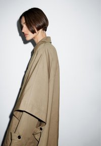 Beige übergroßes Hemd mit Kragen und weiten Ärmeln, mit Knopfdetails und einem glatten, strukturierten Stoff.