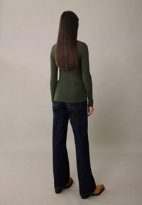 Olivegrünes, geripptes Langarmoberteil, kombiniert mit dunkelblauen, ausgestellten Jeans. Das Oberteil sitzt enganliegend, während die Jeans ein klassisches Fünf-Taschen-Design aufweisen.