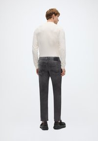 Γκρι τζιν παντελόνι από τζιν ύφασμα με ίσια γραμμή, συνδυασμένο με κρεμ μακρυμάνικη μπλούζα. Διαθέτει ελάχιστες ραφές και πίσω πατζάκι. Μαύρα παπούτσια ολοκληρώνουν το ντύσιμο.