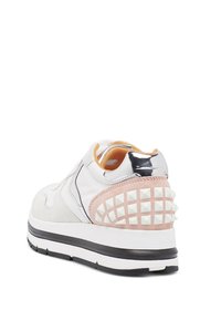 White sneaker featuring suede and leather materials, a pink suede heel with white studs, and a shiny silver accent on the back.