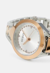 Orologio in oro rosa e finitura argento con cassa rotonda, quadrante argentato, indicatori delle ore a forma triangolare e design del bracciale a maglie.