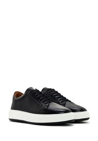 Black leather sneakers with a smooth finish, round toe, lace-up design, and contrasting white rubber sole. Accented with a tan interior.