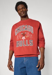 Sweatshirt rouge avec l'inscription "CHICAGO BULLS" en lettres blanches et noires, accents floraux et logo de taureau ; poignets et encolure côtelés.