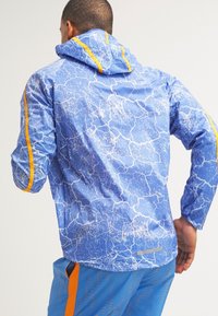 Veste légère bleue avec un motif craquelé, des accents orange sur la capuche et les manches, ainsi qu'un détail réfléchissant à l'arrière.