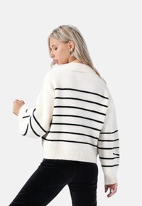 Strikkegenser i krem med svarte horisontale striper, med bred krage og løse ermer, laget av myk teksturert stoff.