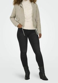 Light beige bomber jacket with drawstrings, paired with a cream knitted sweater and black skinny jeans. Black ankle boots complete the look.