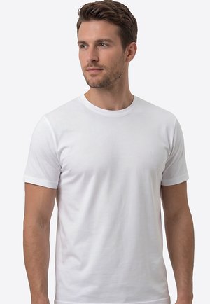 Man with short brown hair and beard wearing a plain white short-sleeve t-shirt, looking slightly left on a light background.