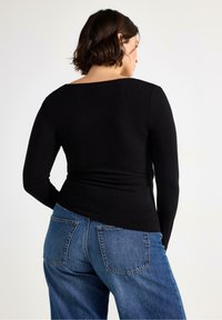 Svart långärmad topp med bred halsringning och åtsittande midjeband, kombinerad med lösa blå jeans i denim med två bakfickor.