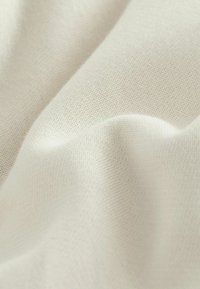 Tessuto di cotone color crema con una superficie liscia, che presenta pieghe morbide e un motivo di tessitura fine e uniforme.