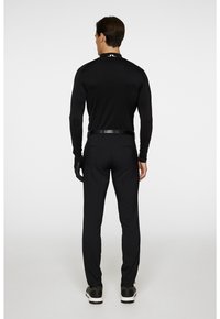 Svart långärmad topp, figurnära design, tillsammans med svarta byxor och ett svart bälte. Svarta handskar och sneakers fulländar outfiten. Minimalistisk stil.