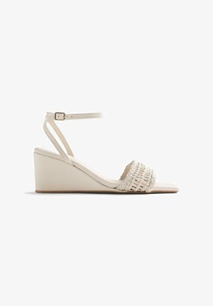 Sandalia blanca de cuña con tira frontal tejida y correa con hebilla en el tobillo, con tacón bajo y diseño de punta abierta.