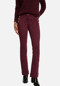 Jeans droit bordeaux en coton, avec des boutons sur les côtés, une texture lisse et une coupe classique, associés à un pull en maille.