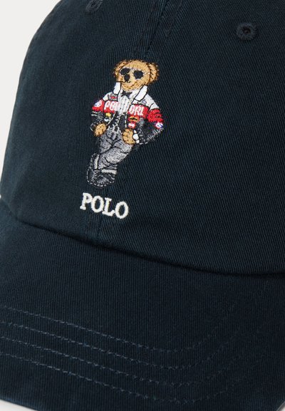 Black cap with embroidered teddy bear wearing sunglasses, jacket, and pants above the word Polo in white stitching.