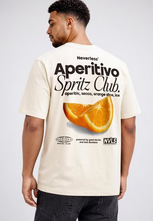 Mann trägt ein beiges T-Shirt mit dem Schriftzug "Aperitivo Spritz Club" und einer Grafik einer Orangenscheibe auf dem Rücken.