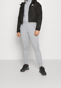 Svart kort jacka, grå zip-up sweatshirtoch grå sweatpants. Svarta och grå träningsskor. Slät tyg, åtsittande form, minimal märkning.