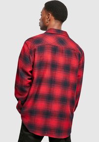 Chemise en flanelle écossaise rouge et noire avec col pointu, poignets à boutons et coupe décontractée. Présente un ourlet arrondi et un tissu texturé.