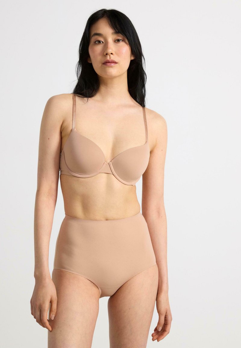 Beige rinta, jossa on sileä pinta ja ohuet olkaimet, yhdistettynä korkea vyötäröinen beige alushousu; molemmat esittelevät minimalistista muotoilua ja saumatonta viimeistelyä.
