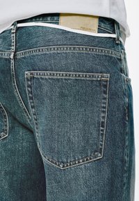 Jeans aus Denim in mittlerem Blau, mit einem traditionellen Fünf-Taschen-Design, sichtbaren Nähten und einem hellbraunen Etikett am Bund.